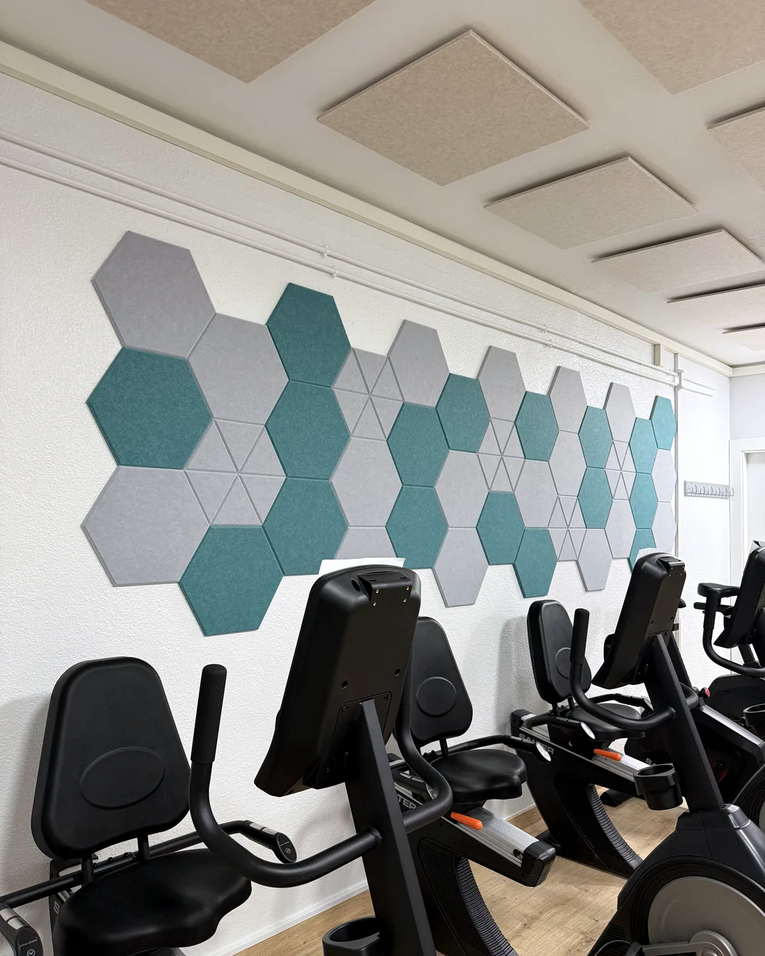 Gimnasio con paneles acústicos hexagonales verdes y grises tras las bicicletas estáticas