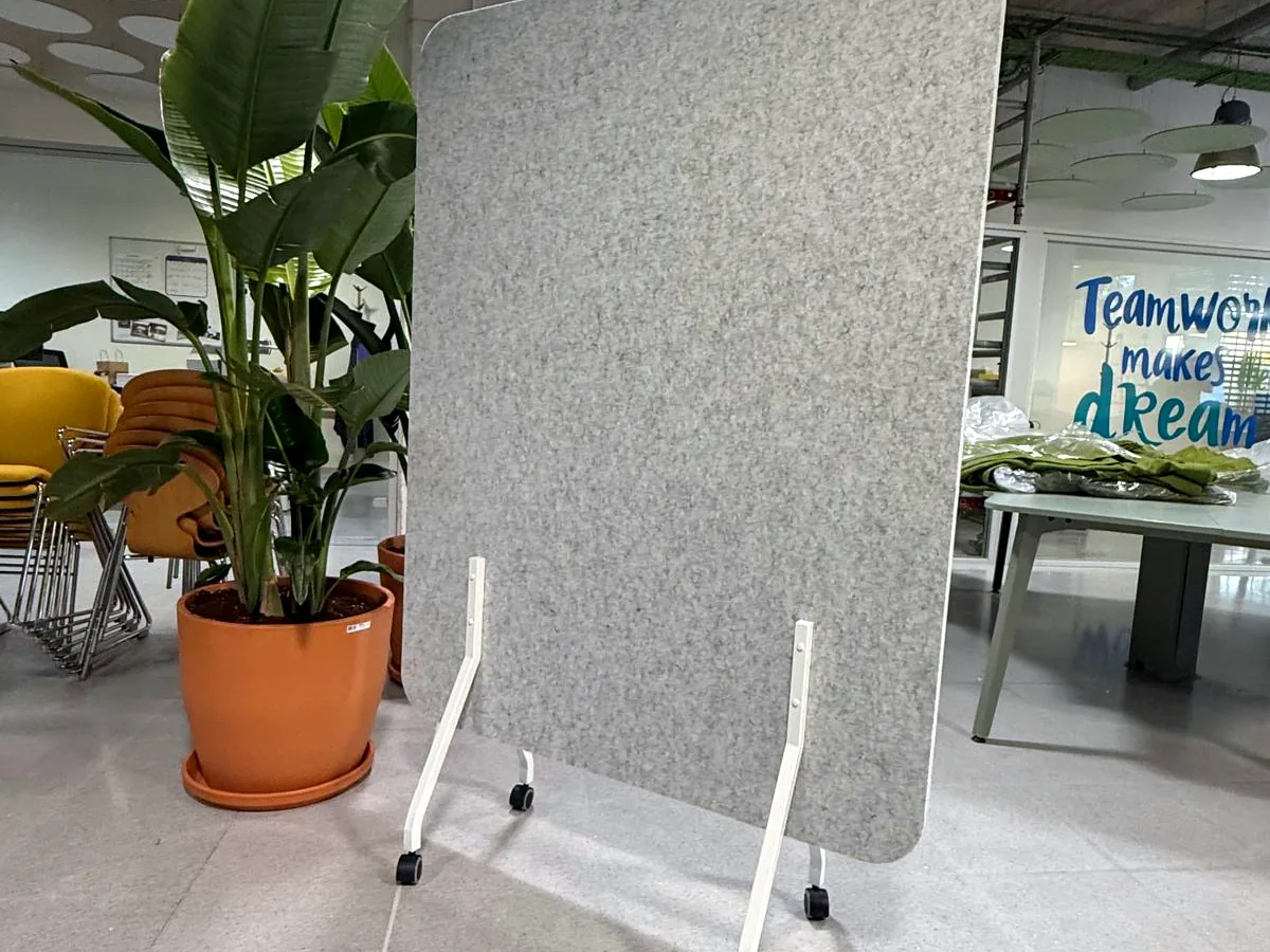 Biombo acústico gris junto a una planta en una oficina
