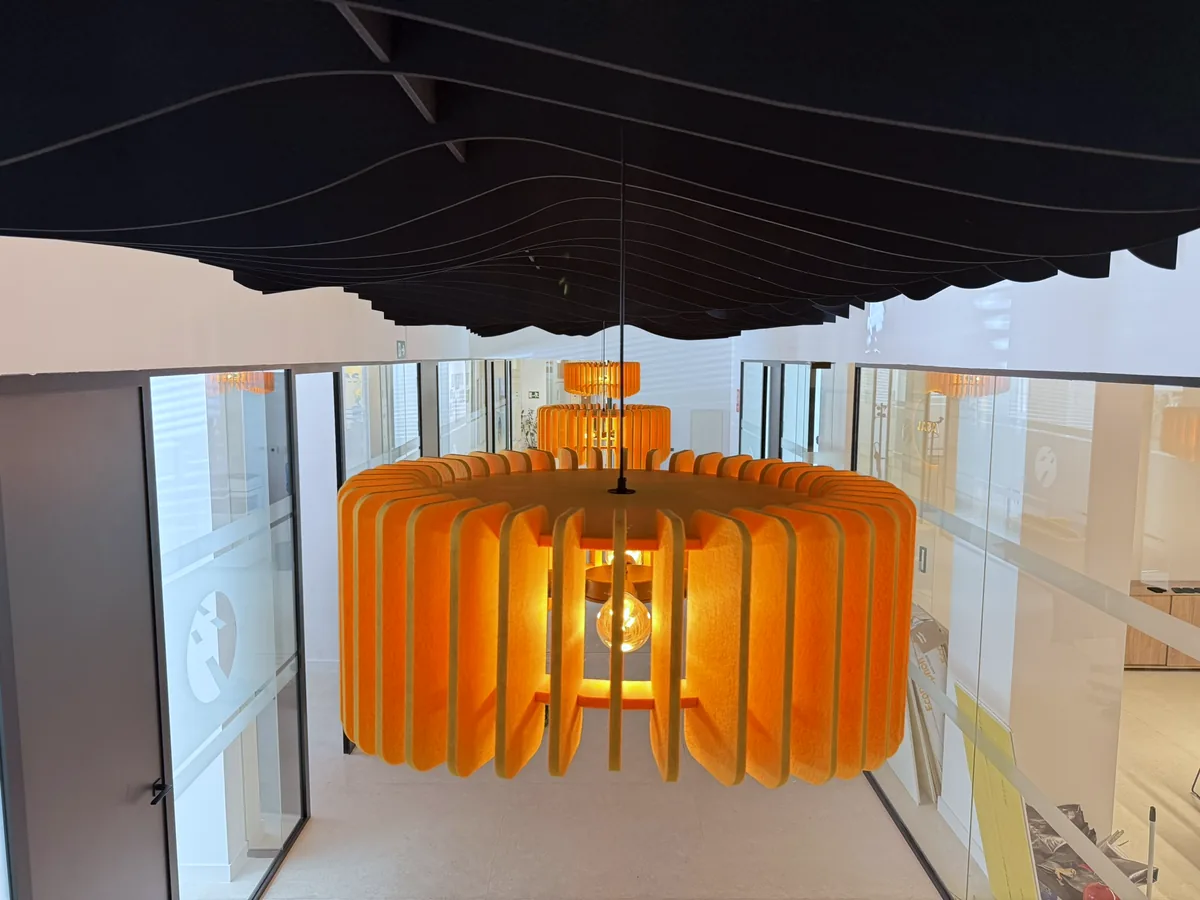 Luminaria acústica de lamas naranjas suspendida bajo un techo de baffles negros