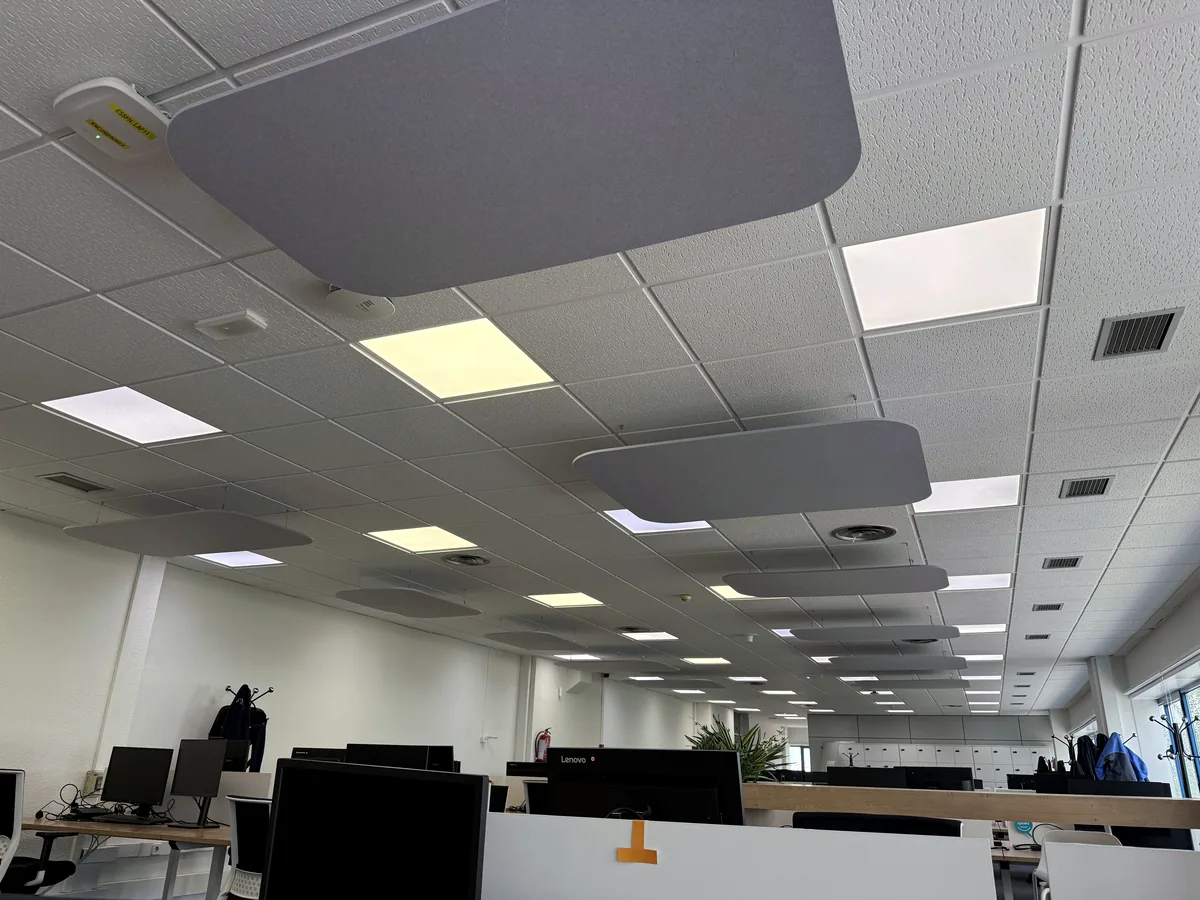 Oficina en planta abierta con nubes acústicas grises suspendidas del techo