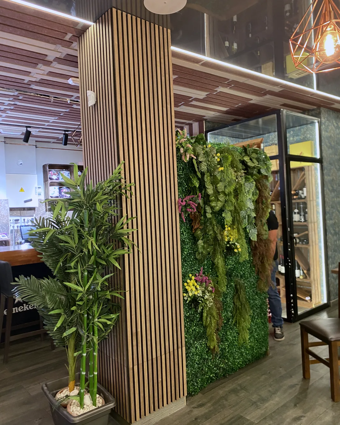 Comercio con revestimiento de lamas, jardín vertical y luminarias colgantes