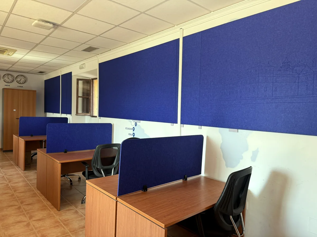 Oficina con separadores acústicos azules sobre las mesas y paneles azules en la pared