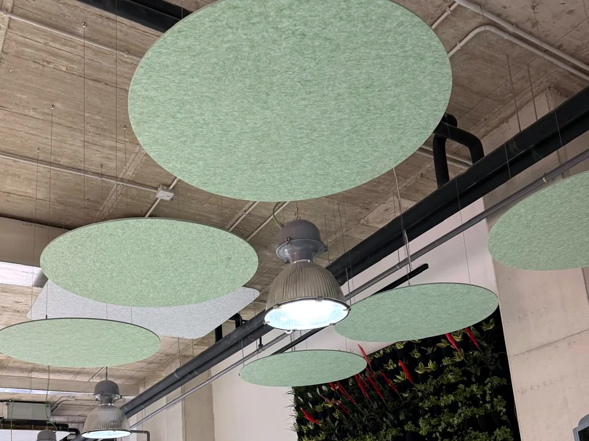 Nubes acústicas circulares verdes suspendidas junto a un jardín vertical