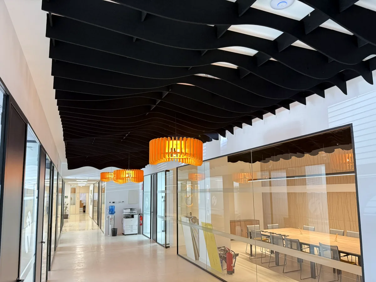 Pasillo de oficinas con baffles acústicos negros en ondas y lámparas naranjas