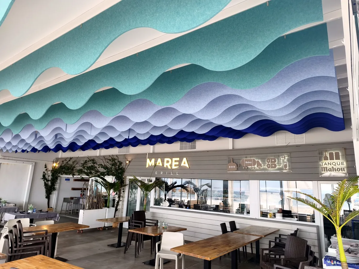 Techo acústico en olas de PET turquesa y azul sobre el comedor de Marea Grill